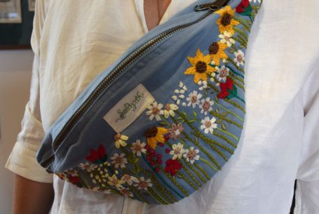Bauchtasche mit buntem Blumen- und Sonnenmuster auf blauem Hintergrund.
