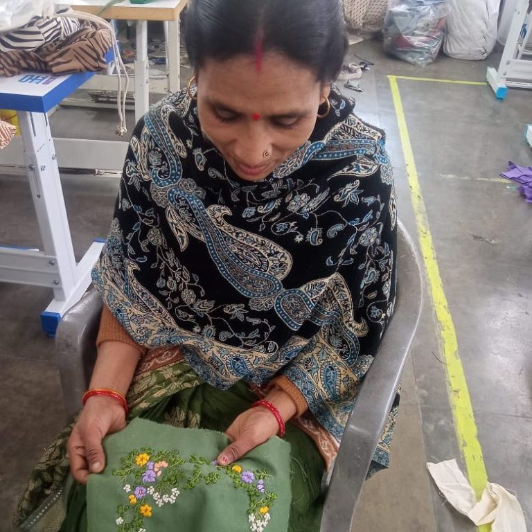 Frau näht an einer Nähmaschine mit bunten Stickereien auf einem Stoff.